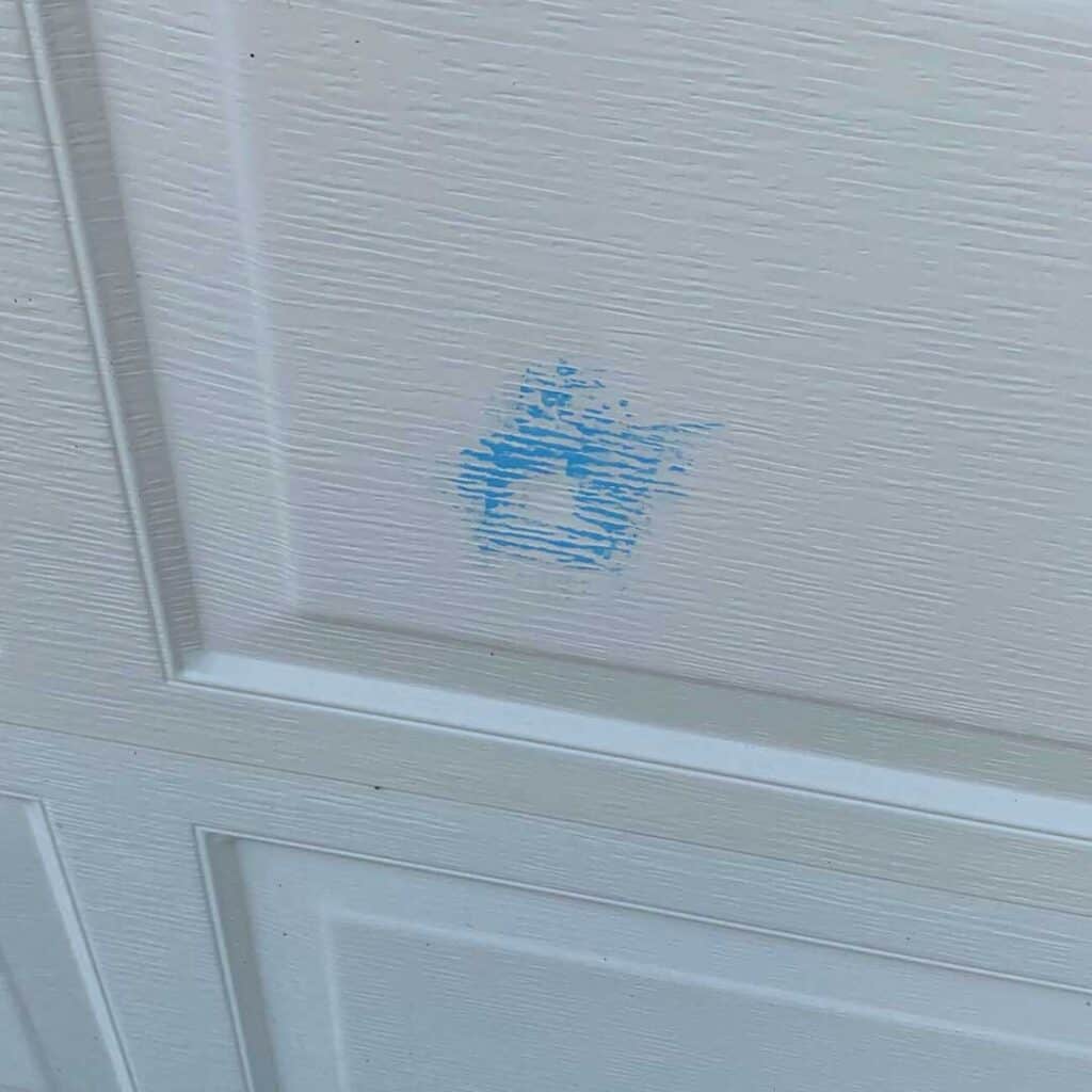 Hail damage on garage door highlighted by roofer chalk