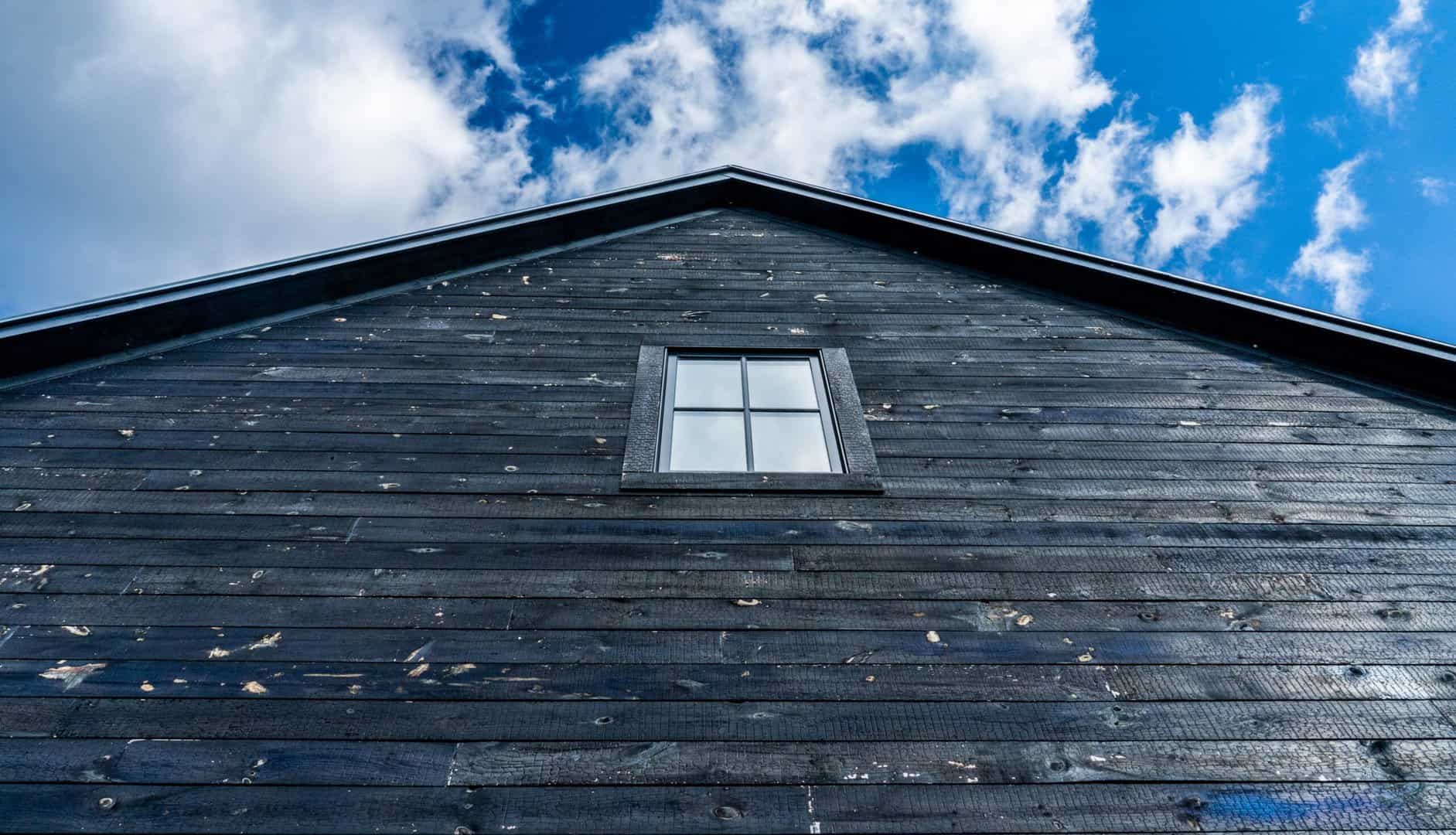 close up cropped image St. Paul Home with painted dark wood siding with roof peak against blue sky with white clouds