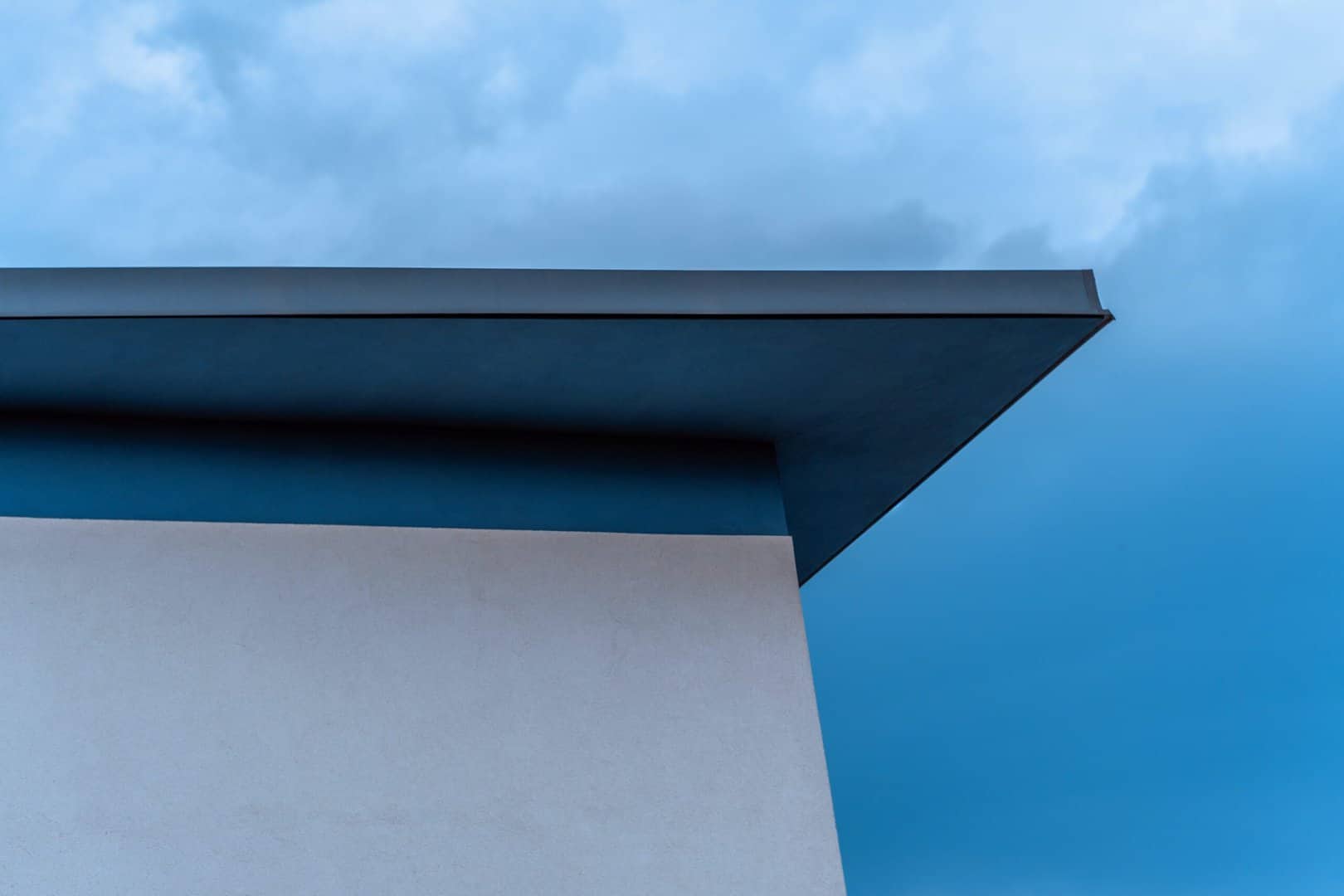 A flat roof with a partly cloudy sky behind it.